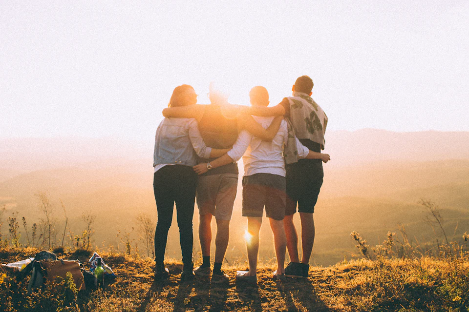 Four person hands wrap around shoulders while looking at sunset