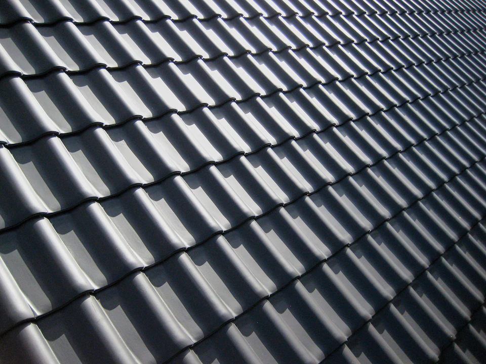A pattern of dark grey roof tiles with sharp shadows in bright light
