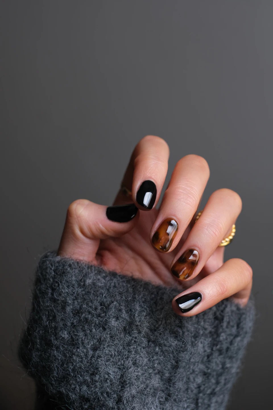 A hand with black and tortoiseshell patterned nails wearing a gold ring