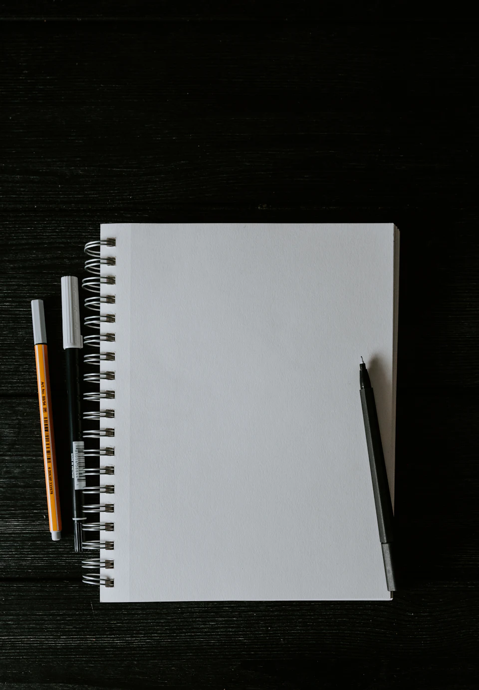 White spiral notebook beside orange pen