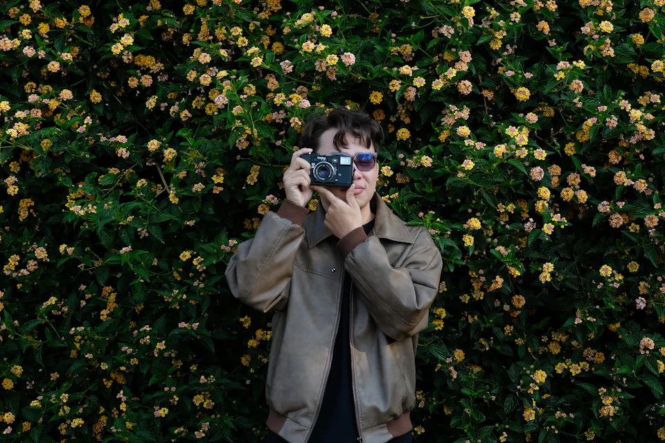 Person holding vintage camera in front of blooming flowers