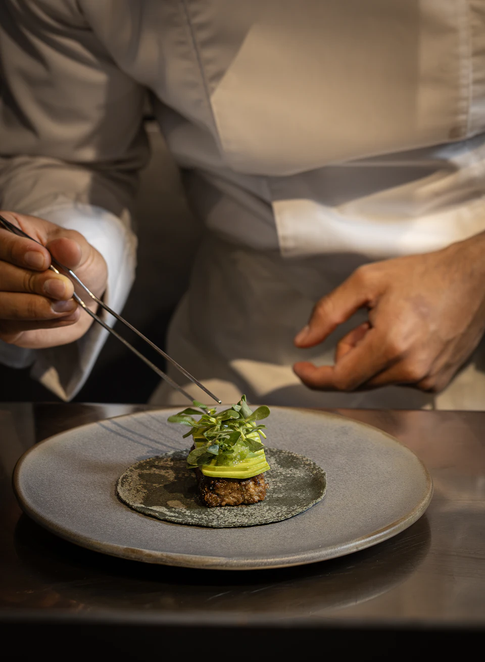 Chef garnishing a small dish with fresh greens